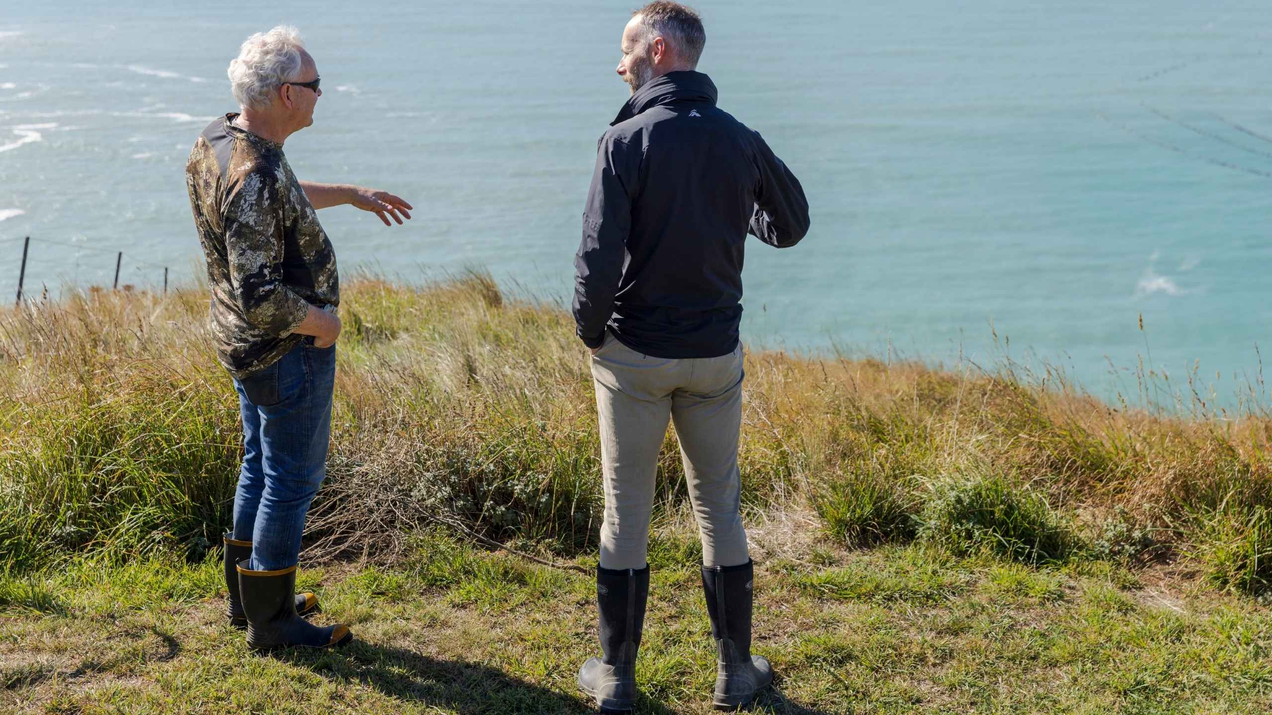 Two people standing on a grassy hill overlooking a body of water.